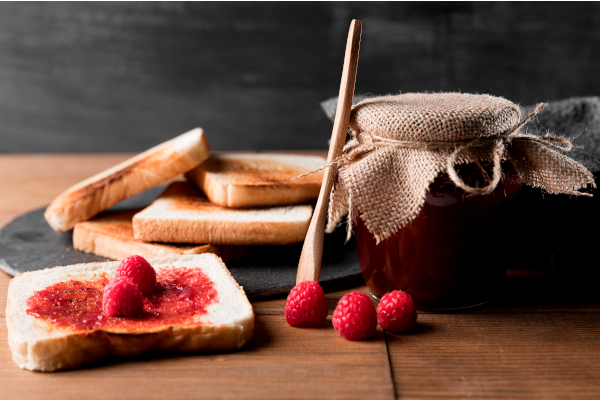 Vasetto di marmellata e confettura alla lamponi accompagnata da cucchiaio di legno e toast con marmellata spalmata